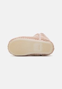Light pink slipper with textured upper, white stitching details, and rubber sole featuring a wavy pattern for grip.