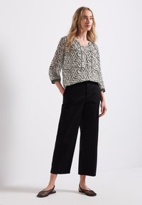 Blusa leggera a fantasia con scollatura a V e maniche a tre quarti, abbinata a pantaloni neri larghi e scarpe slip-on in rete.
