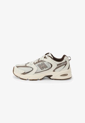 Zapatilla deportiva blanca y marrón con parte superior de malla, diseño curvado, suela acolchada y logo "N" en el lateral. Suela exterior de goma duradera.