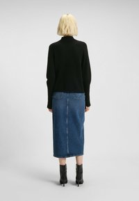 Schwarzer Strickpullover, Jeans-Midirock und schwarze Knöchelstiefel. Der Pullover hat einen hohen Kragen; der Rock verfügt über aufgesetzte Taschen auf der Rückseite und ist gerade geschnitten.