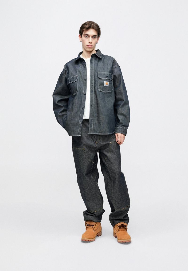 Mørk denimjakke med store forlommer, knaplukning og kontrasterende syninger. Kombineret med løstsiddende mørke jeans og tanfarvede støvler.