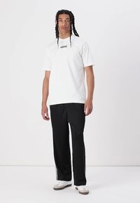 Hvit kortermet t-skjorte med svart "adidas"-logo, kombinert med svarte joggebukser med hvite sidestriper og hvite sneakers.