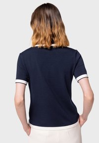 Mörkblå piké med kort ärm och vit kant vid kragen och ärmarna. Åtsittande design med en texturerad yta och en lätt glans.