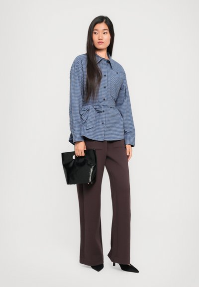 Sinine ruuduline särk nuppudega ja seotud vöökoht, koos pruunide kõrge vöökohaga laiaäärsetega pükstega ja musta läikiva käekotiga.