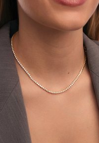Collana in tono oro caratterizzata da una fila di piccoli strass trasparenti distribuiti uniformemente lungo una catena liscia, evidenziando la sua lucentezza e design elegante.
