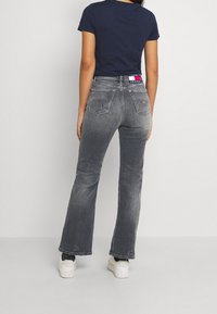 Dark gray flared jeans with a distressed texture, visible pockets, and a waistband accent featuring logo design; paired with white shoes.