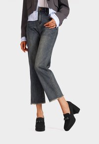 Jeans in denim blu a vita alta con gamba dritta e orlo sfilacciato, abbinati a mocassini neri con dettaglio a catena.