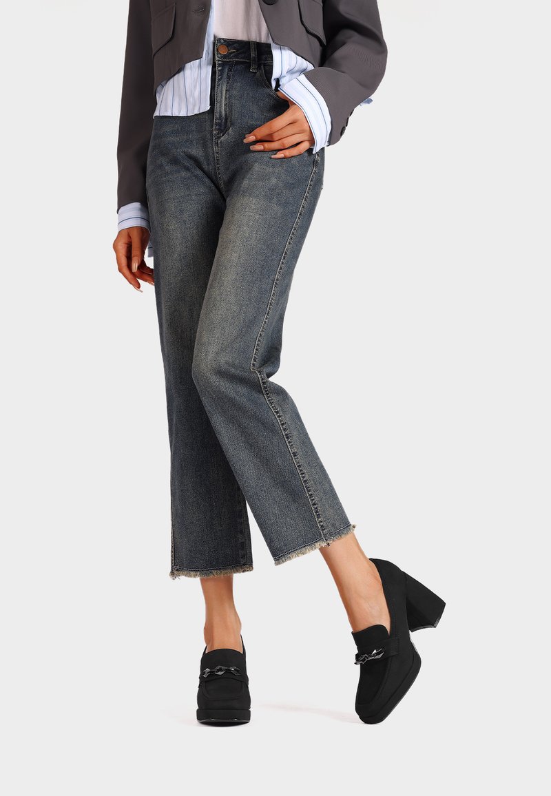 Jeans in denim blu a vita alta con gamba dritta e orlo sfilacciato, abbinati a mocassini neri con dettaglio a catena.
