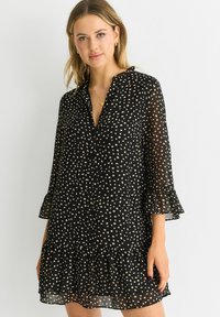 Black dress with white polka dots, long sleeves with ruffle cuffs, and a tiered hem. Made from lightweight, sheer fabric. Button front.