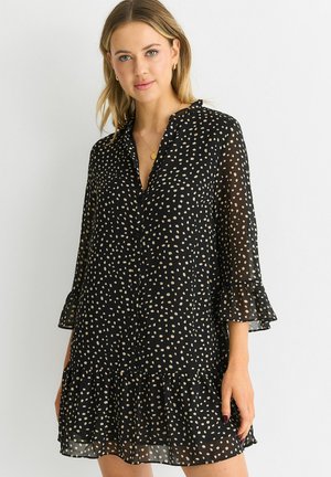 Black dress with white polka dots, long sleeves with ruffle cuffs, and a tiered hem. Made from lightweight, sheer fabric. Button front.