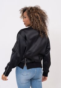 Zwart satijnen bomberjack met geribde mouwen en zoom, voorzien van ritszakken aan de zijkanten en een relaxte pasvorm.