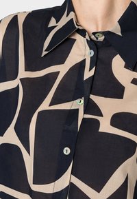 Colletto e camicia con bottoni caratterizzati da grandi forme geometriche astratte in nero e beige su tessuto leggero.