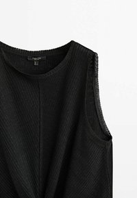 Haut sans manches noir avec une texture côtelée, encolure ronde et un détail de nœud à l'avant. Fabriqué en tissu léger.