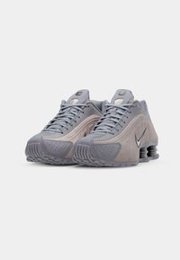 Pilko odos ir tinklo sportiniai bateliai su tekstūruotu paviršiumi, apvaliu pirštu ir segmentuota kulno dizainu. Savybė - juodas Nike swoosh logotipas.