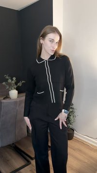 Svart skjorttopp med vit pipning längs kragen och fickorna, kombinerad med svarta byxor. Slät tyg och skräddarsydd design.