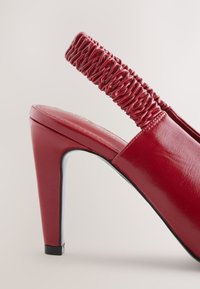 Chaussure à talon haut slingback en cuir rouge avec une bride élastique froncée, un bout pointu et une finition brillante. Accent noir sur la semelle.