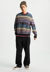 Multi-stripe knit sweater in blue, pink, green, and brown, paired with black pants and brown sneakers. Topped with a brown knit beanie.