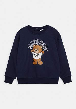 Sweat-shirt bleu marine avec un ours en peluche portant une chemise blanche sur laquelle est écrit "jouet" et le mot "Moschino" au-dessus de l'ours.