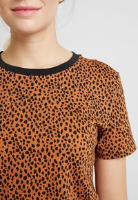 Hnědý tričko s krátkým rukávem s černým leopardím vzorem a černým žebrovaným výstřihem. Jemný textilní materiál.
