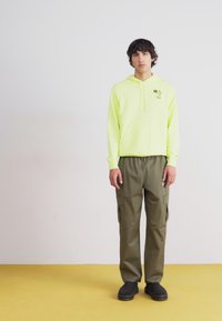 Νεον κίτρινη φούτερ με καγκουρό τσέπη, συνδυασμένη με ελιξ κίτρινα cargo παντελόνια που διαθέτουν πλαϊνές τσέπες. Συμπληρώνει την εμφάνιση μαύρη επίπεδη υποδήματα.