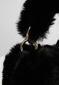 Czarna torebka z futerka ekologicznego o fakturowanej powierzchni. Posiada złoty metalowy pierścień i miękką rączkę. Zaokrąglony kształt, kompaktowy design.