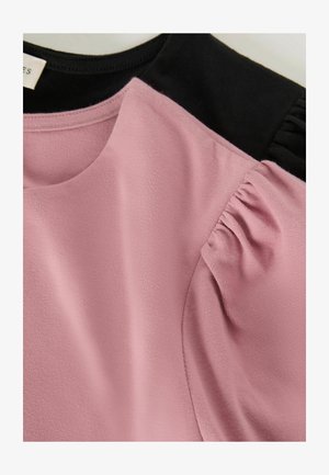 Vaaleanpunainen yläosa mustilla yksityiskohdilla. Pehmeää kangasta, pyöreä pääntie ja kootut yksityiskohdat hihoissa. Sileä pinta, kevyt muotoilu.