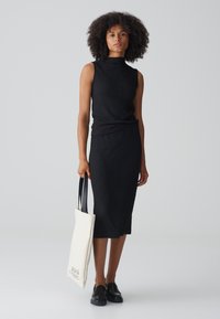 Zwart, gestructureerd tweedelig jurk met een hoge halslijn en een aangesloten silhouet. Inclusief een beige tote bag met zwarte handvatten en tekst.