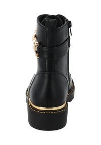 Botín negro de tobillo con parte superior de cuero texturizado, acentos de hardware dorado, cremallera lateral y suela gruesa con un detalle de borde dorado.