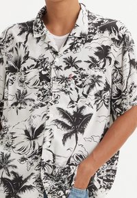 Camicia a maniche corte nera e bianca con motivo floreale tropicale e palme. Presenta una tasca sul petto sinistro e una vestibilità comoda.