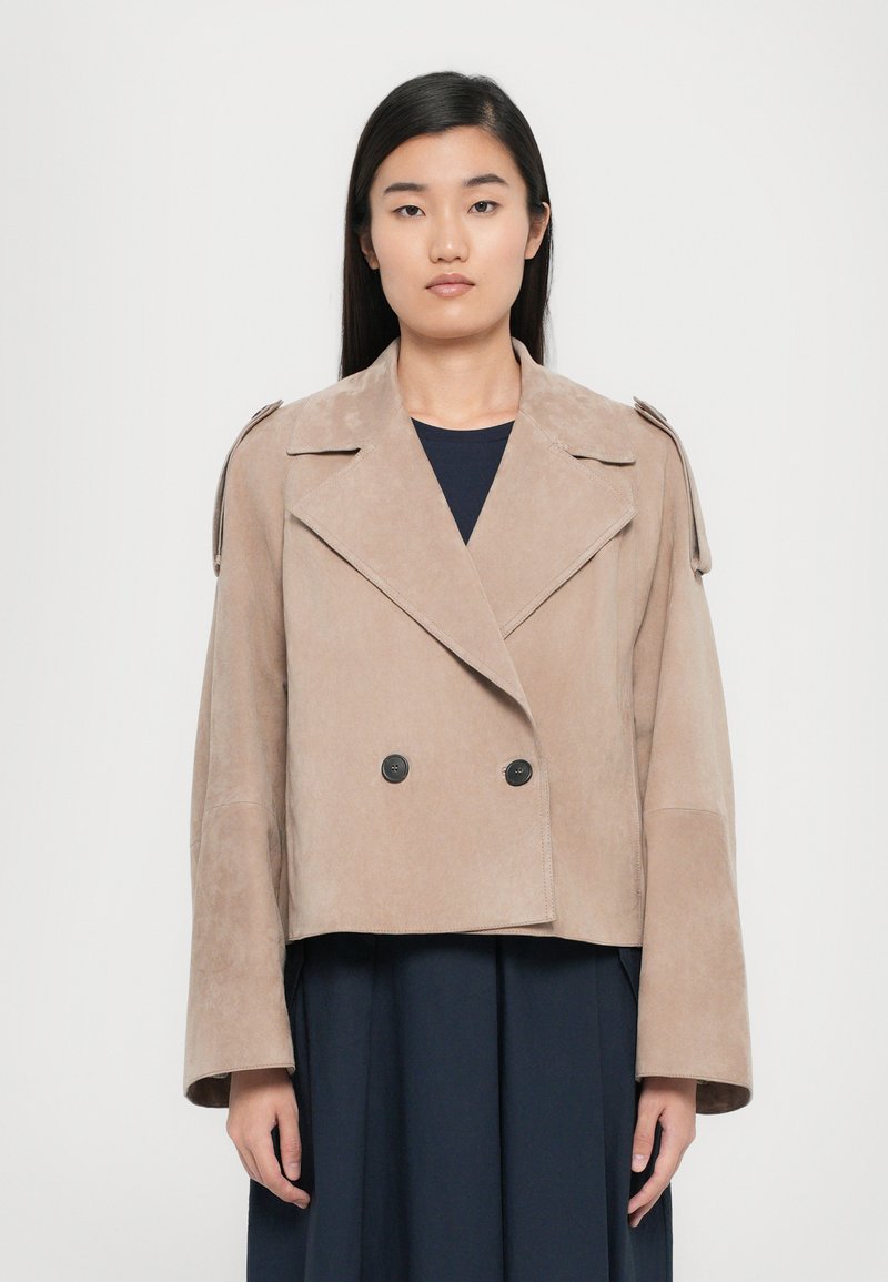 Veste en daim double boutonnage beige clair avec de larges manches et des accents aux épaules, comportant deux boutons noirs à l'avant.