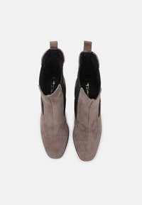 Une paire de bottines en daim taupe avec des panneaux élastiques noirs sur les côtés, des languettes de traction et des bouts carrés, vue d'en haut sur un fond blanc.