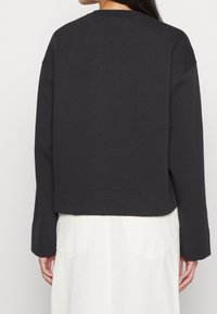 Dark gray cropped sweatshirt with a round neckline and dropped shoulders. Made from soft material, features visible stitching and ribbed cuffs.