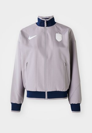 Light gray bomber jacket with a navy collar and cuffs, front zipper, side pockets, and a white logo and emblem on the chest.