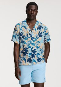 Kortärmad skjorta med knappar i ett blått, gult och beige blommönster. I kombination med ljusblå shorts. Slät tygtextur.