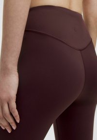 Burgundy legíny s vysokým pasem, vyrobené z hladkého, elastického materiálu s jemnými detaily švů. Detailní pohled na zadní část a pás.