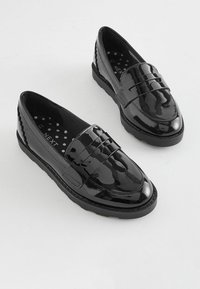 Svarta lackläder loafers med platt gummisole, med en dekorativ rem och texturerade detaljer på baksidan. Innersulan har prickar.