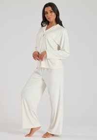 Twee-delig pyjama set in zachte, crème kleurige stof. De top heeft een kraag, knopen en een borstzak; de broek heeft een ontspannen pasvorm.