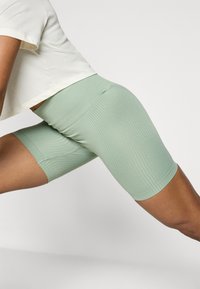 Pantalones cortos deportivos de color verde claro con un cinturón alto. La tela es elástica y suave, diseñada para un movimiento activo y comodidad.