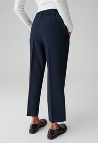Pantaloni navy con vestibilità rilassata, elastico in vita e due tasche posteriori. Tessuto morbido con design a gamba dritta, abbinati a scarpe scure.