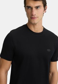 T-shirt in cotone nero con scollo tondo e maniche corte. Dettaglio di logo piccolo sul petto, texture liscia e design aderente.