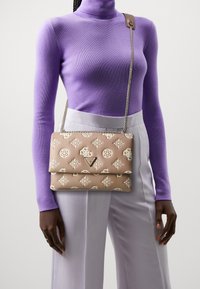 Beige kviltad axelväska med vita mönster, en kedjerem och en triangel-logotypdetalj. Tyget har en mjuk yta.