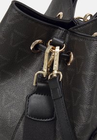 Černá kožená kabelka se zlatými detaily, s texturovaným povrchem, duálními uchy a výrazným logem. Detailní záběr na uzávěr a upevněn í.