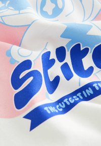 Vitt tyg med en blå och rosa design. Texten säger "Stitch" i fet stil med blå bokstäver, med ett band som står "Den sötaste i."