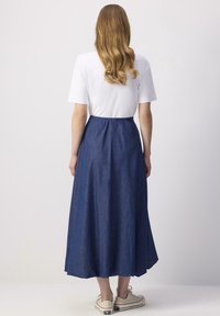 Jupe midi en denim bleu avec une texture lisse, taille froncée et forme évasée. Associée à un haut blanc à manches courtes et des baskets en toile.