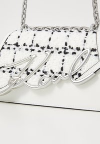 White and black plaid textured handbag featuring a silver chain strap and an oversized silver logo detail on the front.
