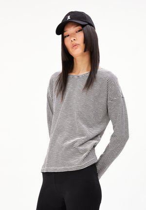 Camicetta a maniche lunghe a righe bianche e nere con una vestibilità rilassata, abbinata a un cappellino nero con un piccolo logo sulla parte anteriore.
