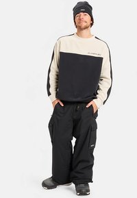 Genser med et kremfarget og svart blokkdesign, kombinert med vide, svarte cargobukser. Komplett med en lue og robuste tursko.