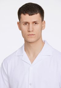 Witte terrycloth shirt met een knoopsluiting aan de voorkant en een kraag, met een zachte textuur en een vereenvoudigd, minimalistisch ontwerp.