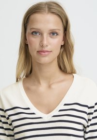 Pull en maille rayé, écru avec des rayures bleu marine, col en V, texture douce, avec une coupe décontractée et des détails minimalistes.