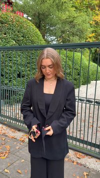 Zwarte oversized blazer met reverskraag, zijzakken en een licht gestructureerde pasvorm. Model houdt een geometrisch gevormde accessoire vast.